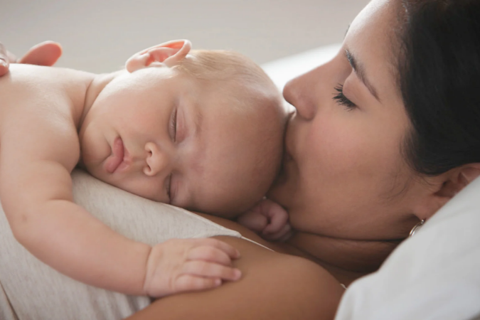 A mother lay down kissing the head of a new born baby lay on her chest